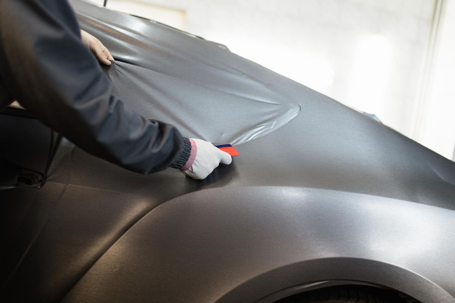 A person is wrapping a car in black vinyl.