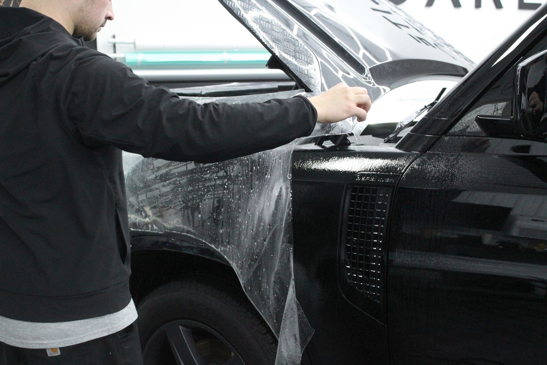 A man is wrapping a black car with plastic wrap.