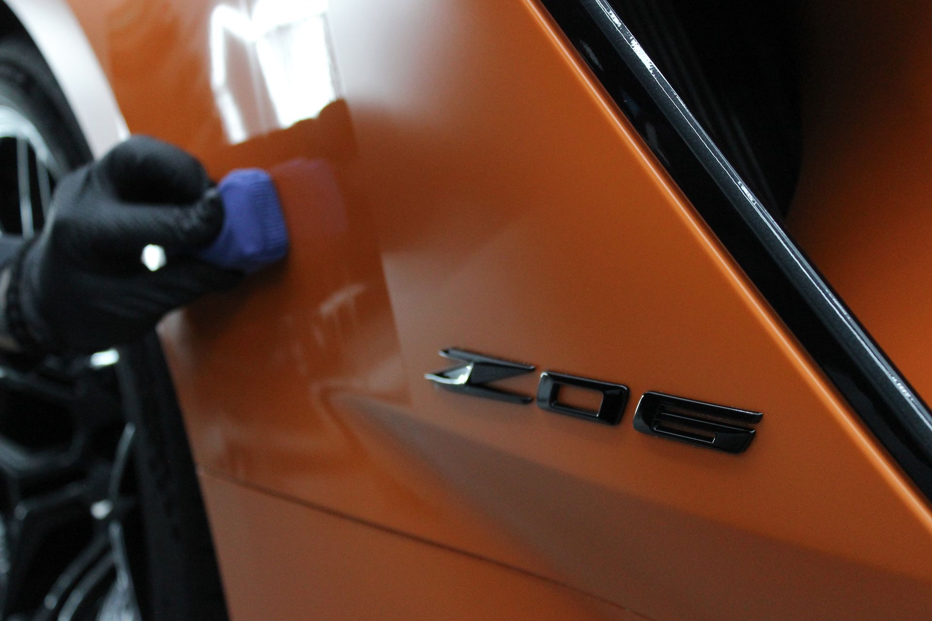 Gloved hand applying product to orange car panel next to a black 