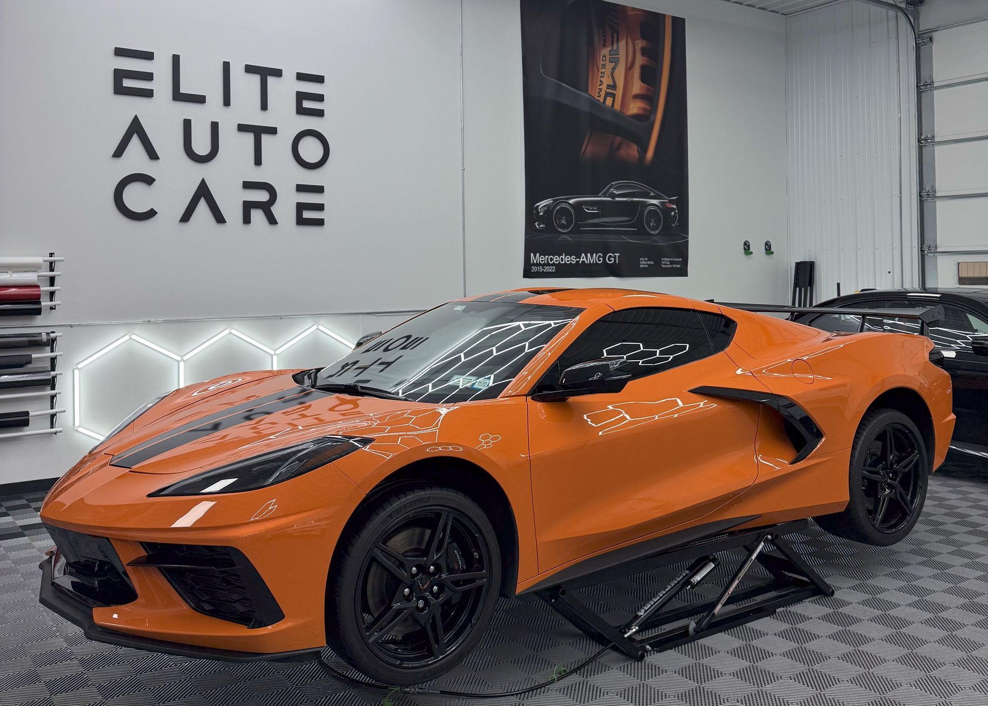An orange corvette is parked on a lift in a garage.