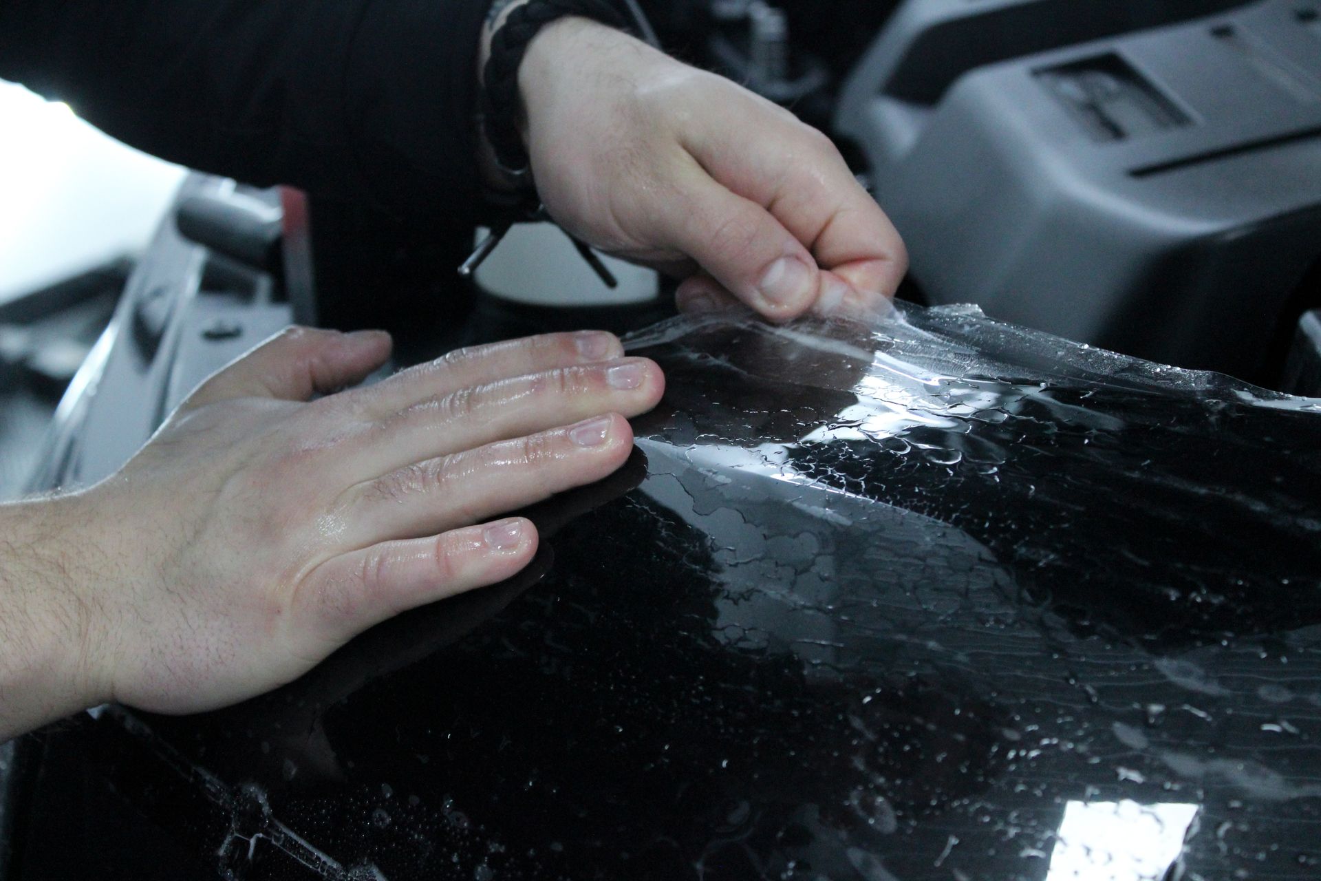A person is applying a clear film to a black car hood.