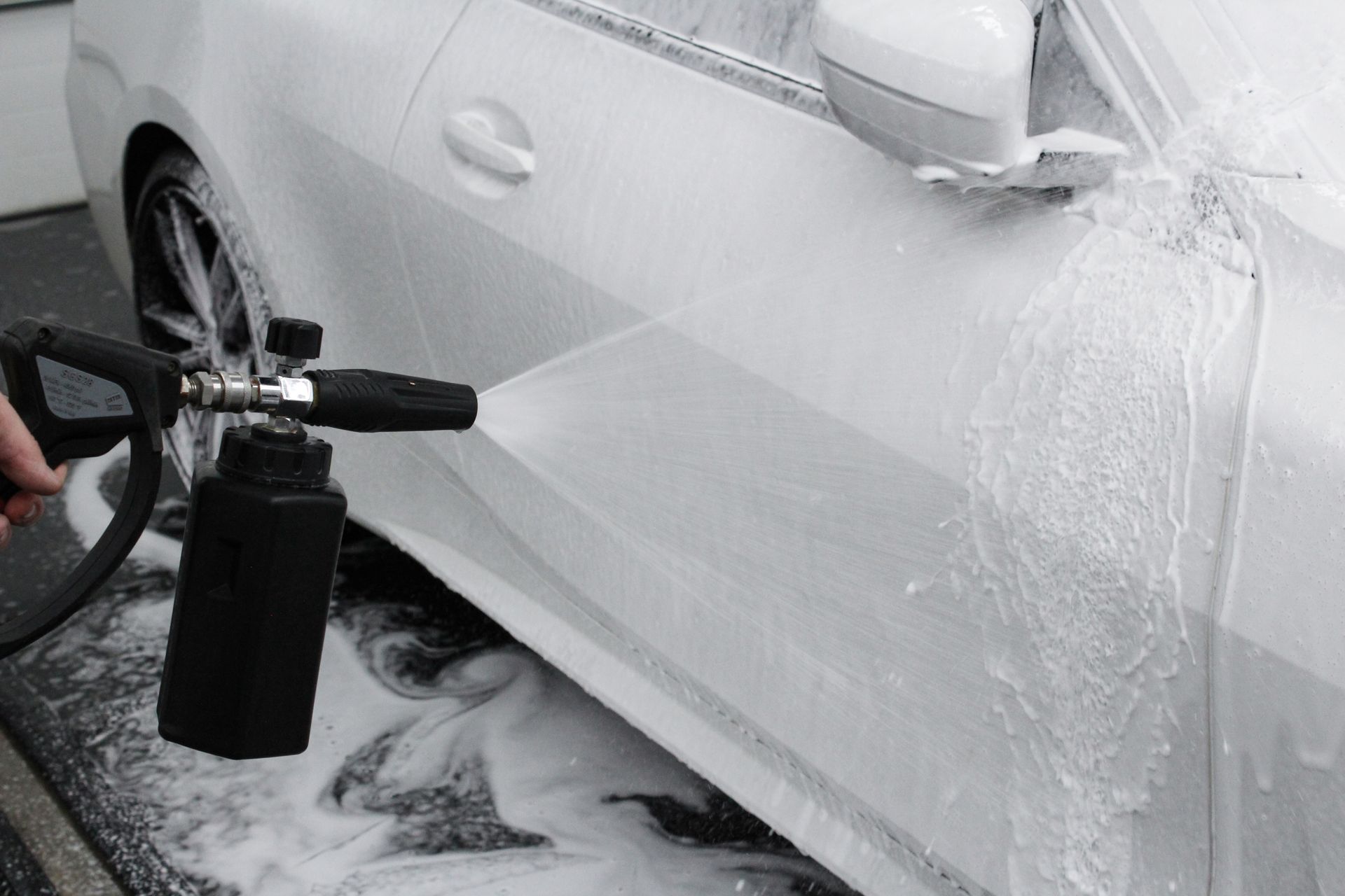 A person is spraying water on a car wheel with a hose.