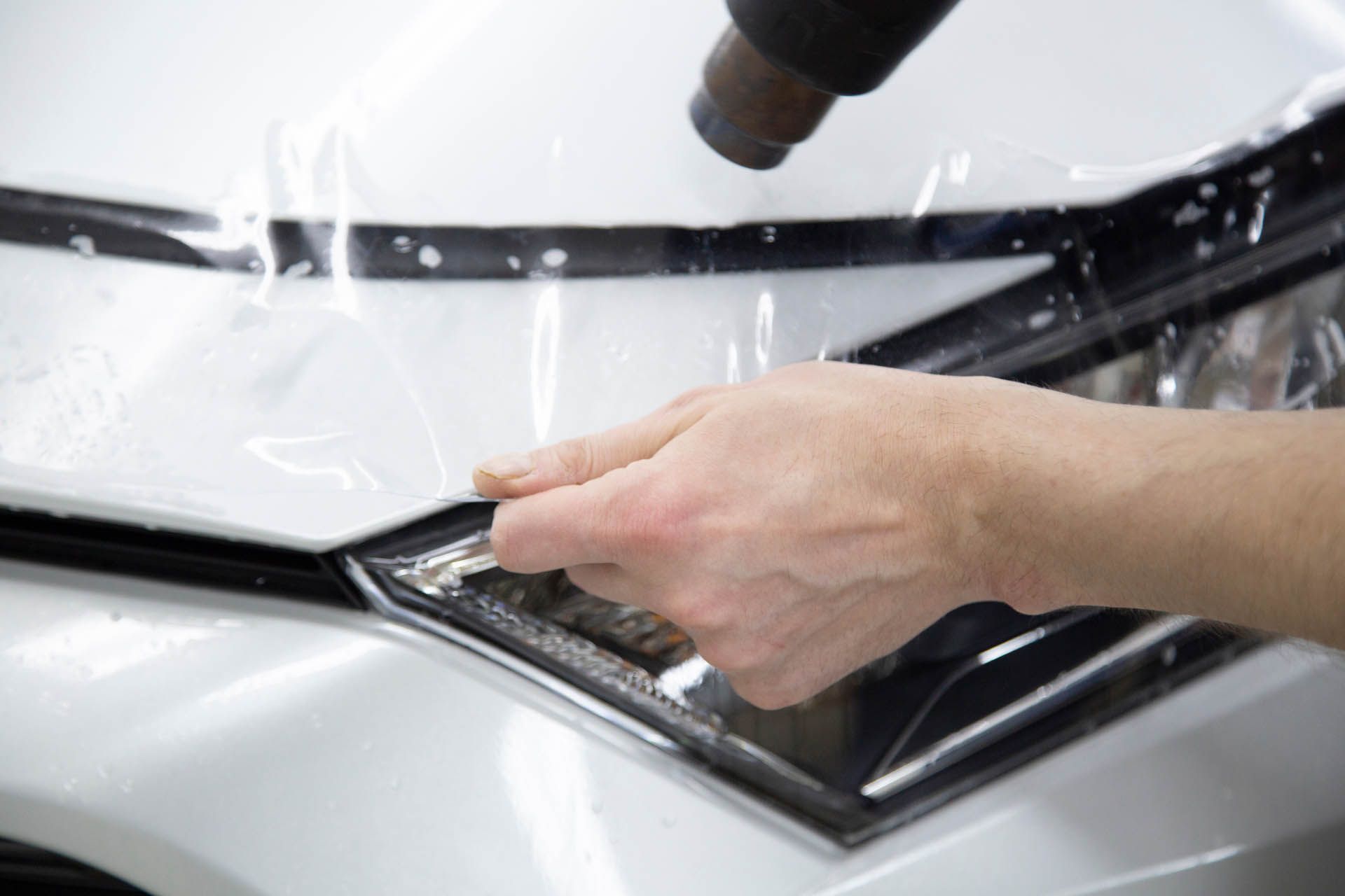 Person applying clear protective film to a car's headlight with a heat gun.