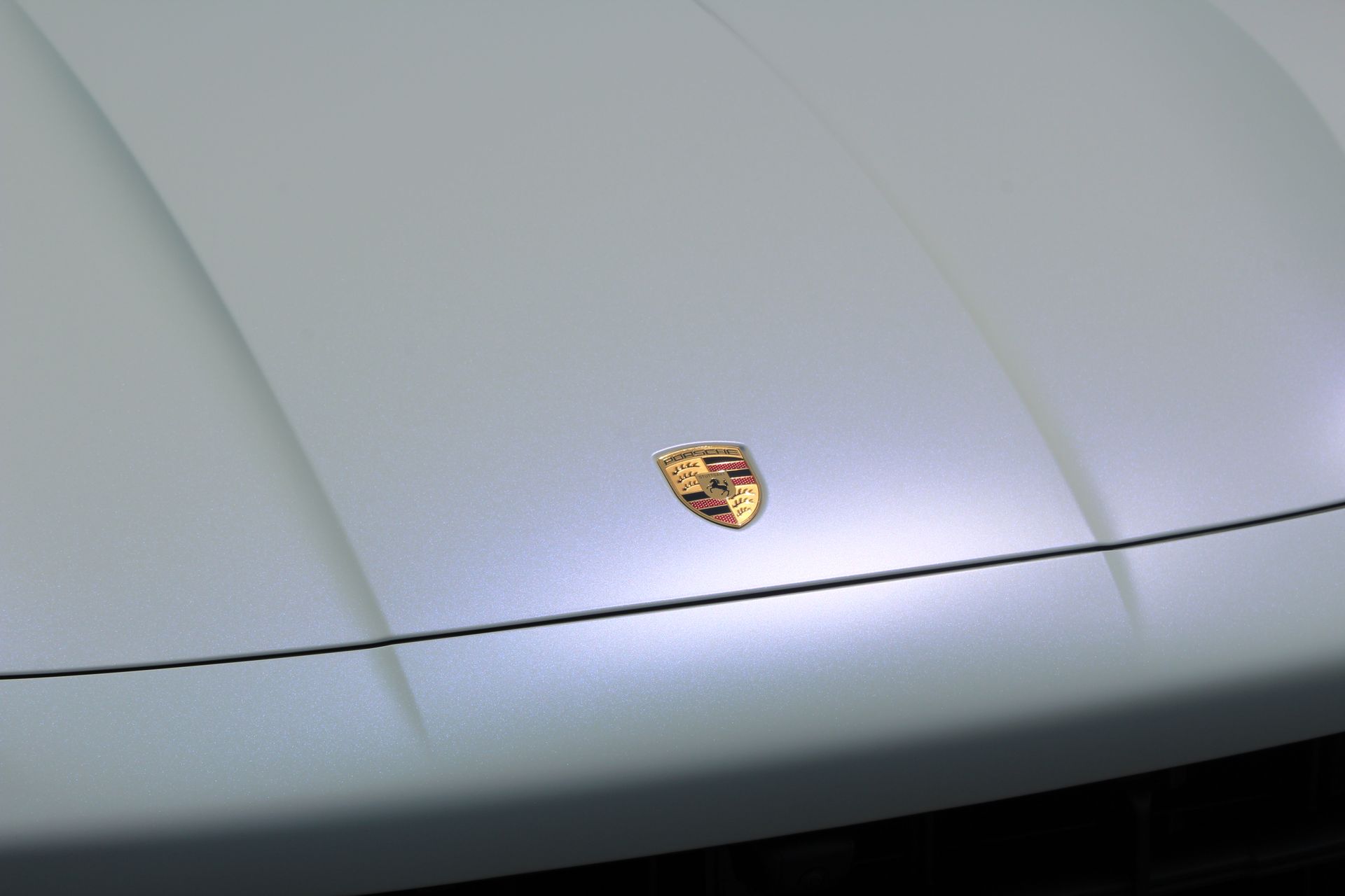 The gold Porsche emblem centered on the matte light gray hood of a car.