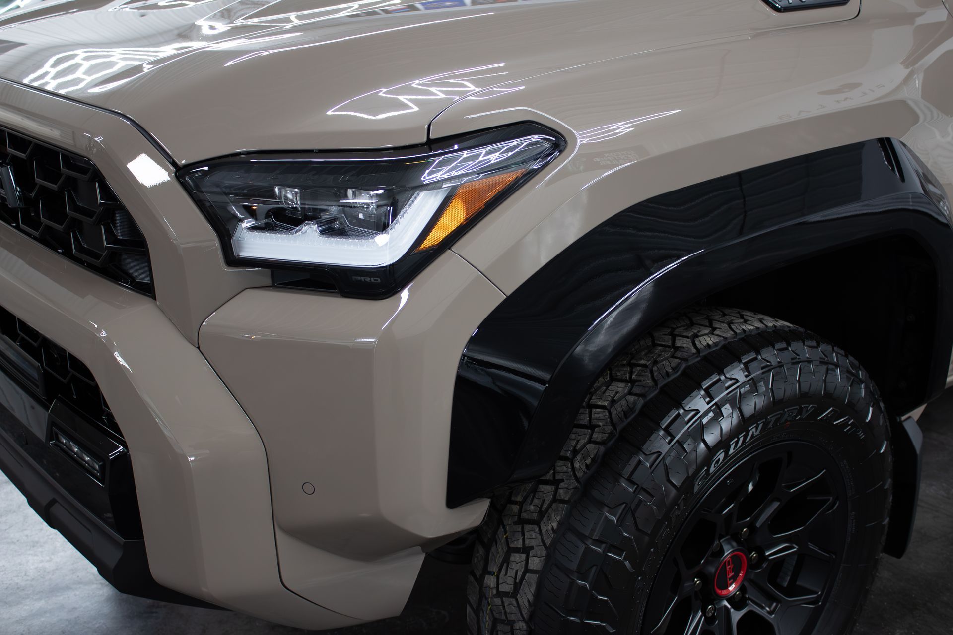 Close-up view of the front driver-side fender, headlight, and black wheel of a tan Toyota Tacoma pickup truck.