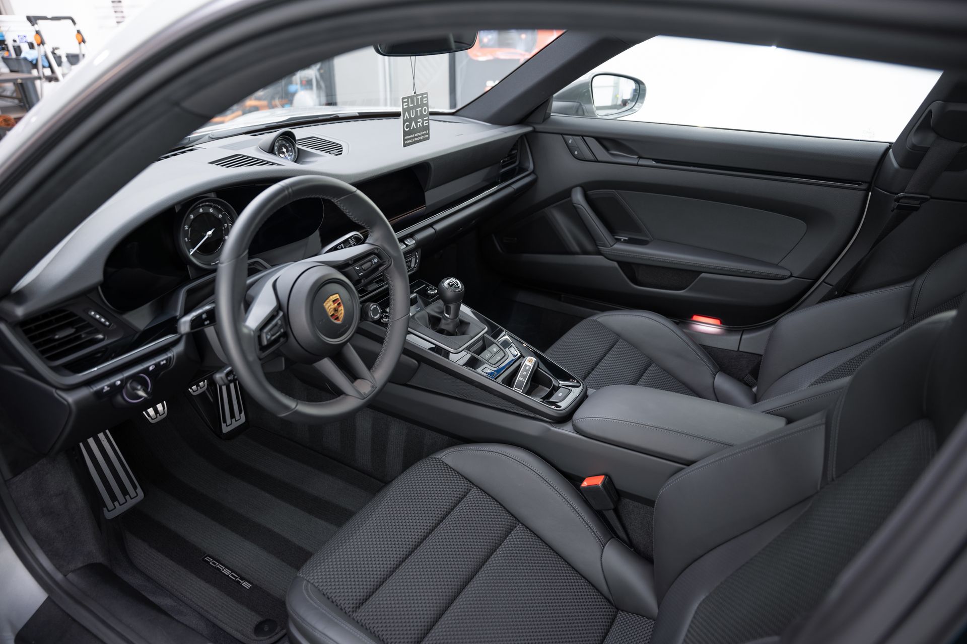 Interior of a black Porsche sports car, featuring a leather steering wheel, bucket seats, and a modern dashboard.