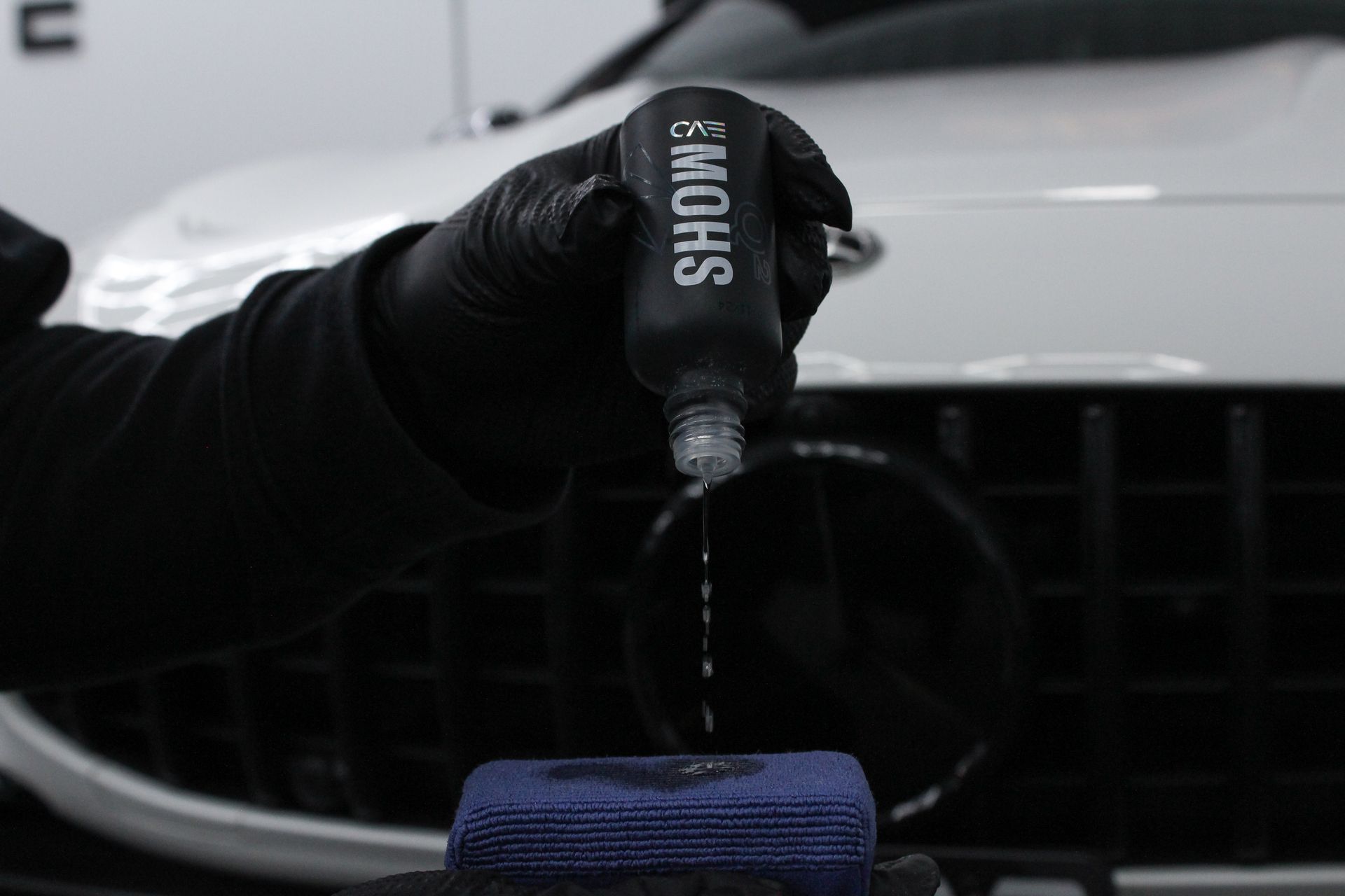A person is holding a blue sponge in front of a car.