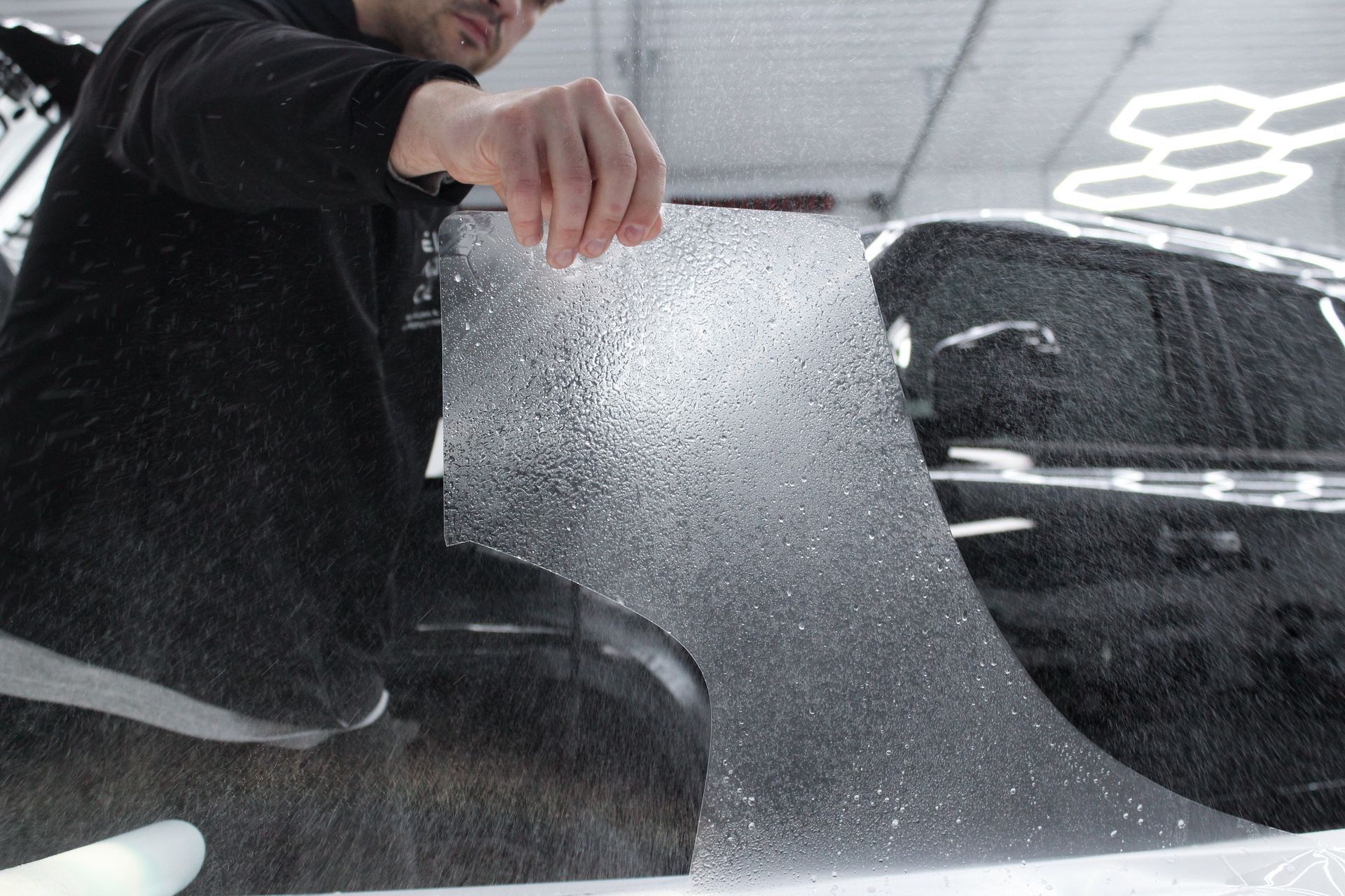 A man is applying a clear film to the windshield of a car.