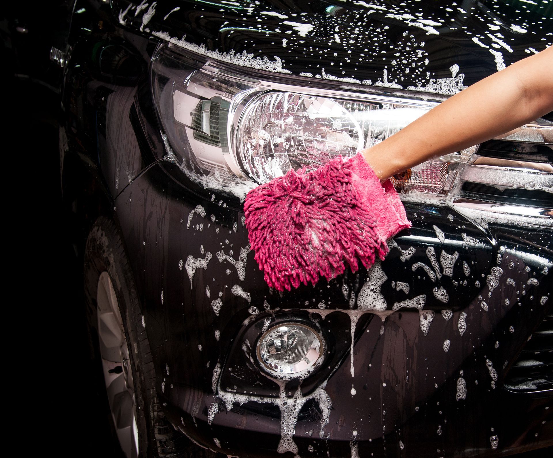 A person is washing a car with a pink glove