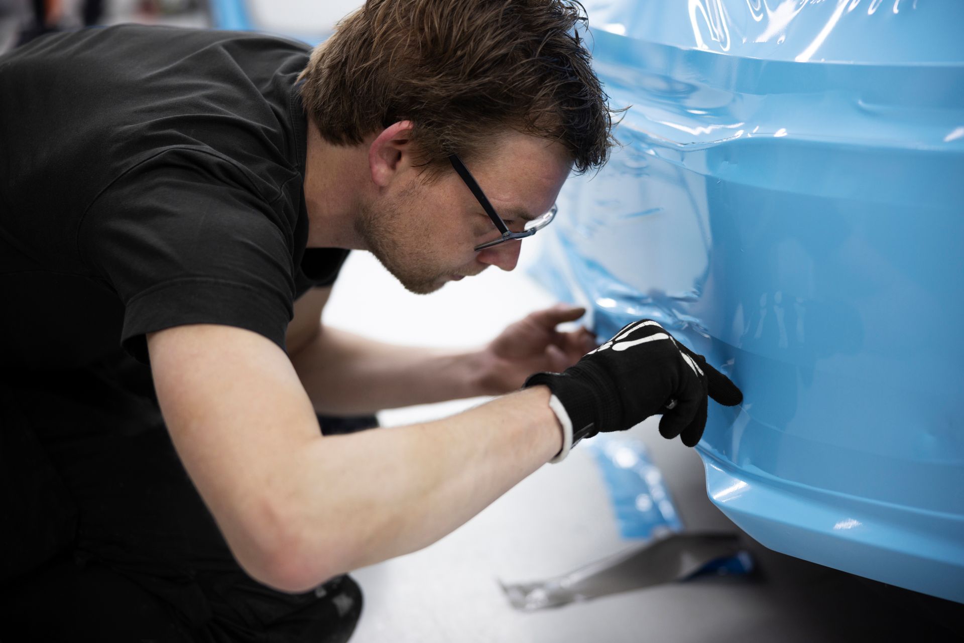 A man in a black shirt is working on a blue car.