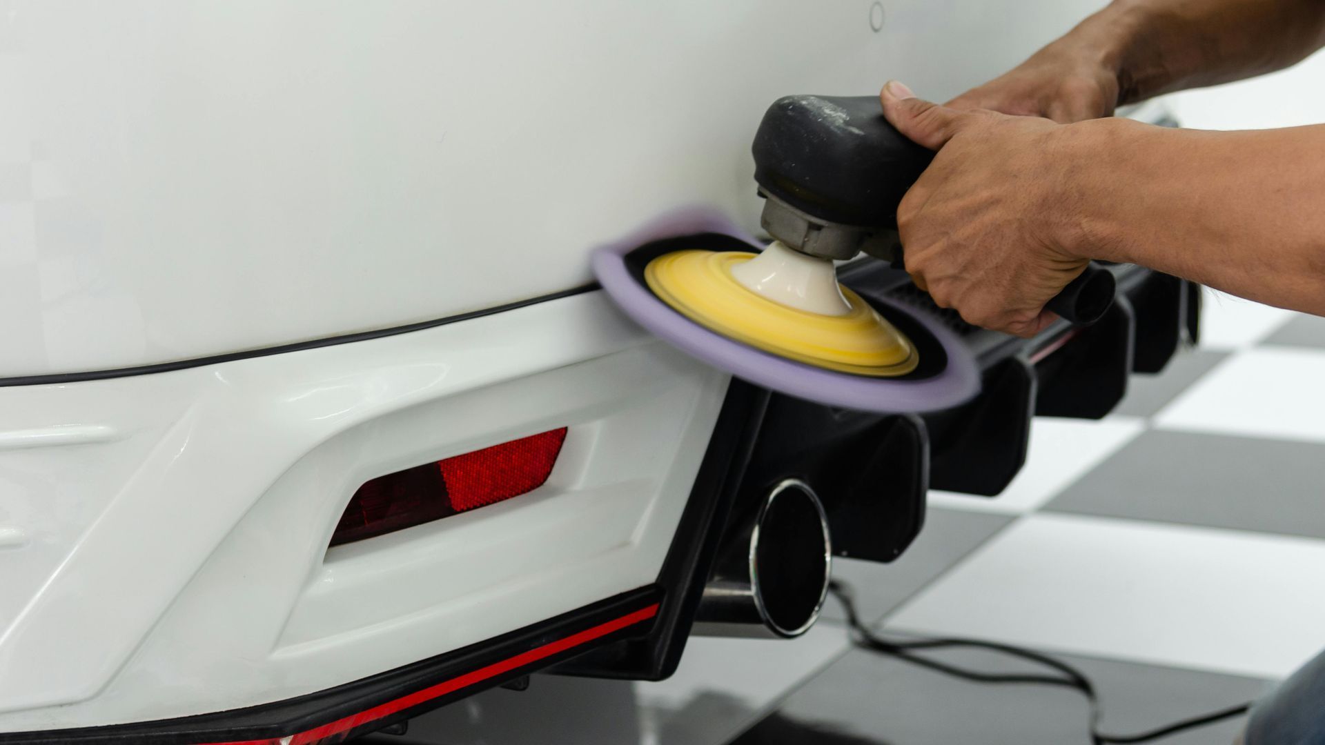 A man is polishing a white car with a machine.
