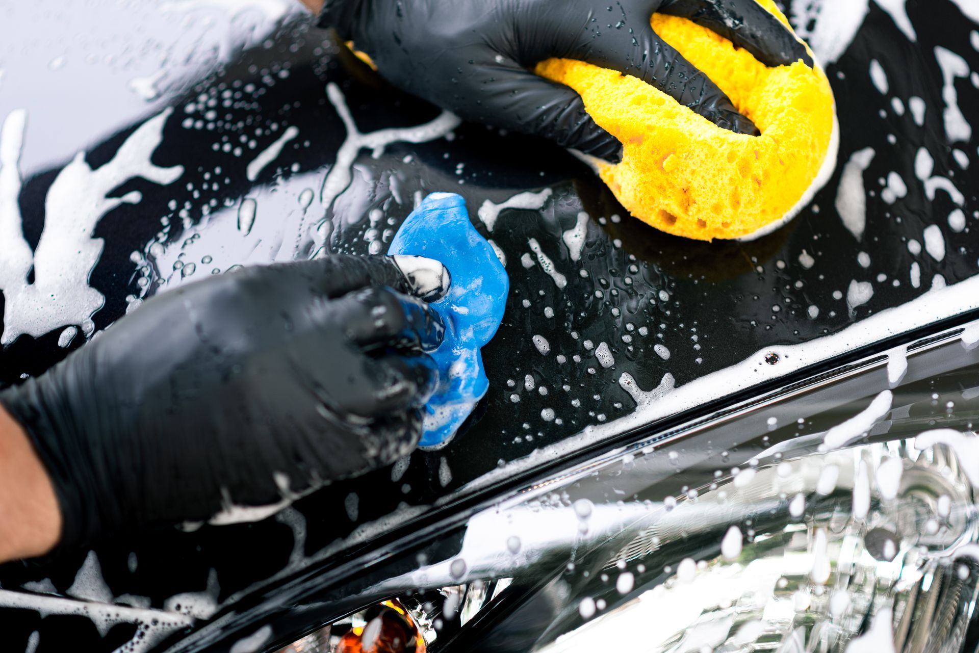 A person is washing a car with a sponge and foam.