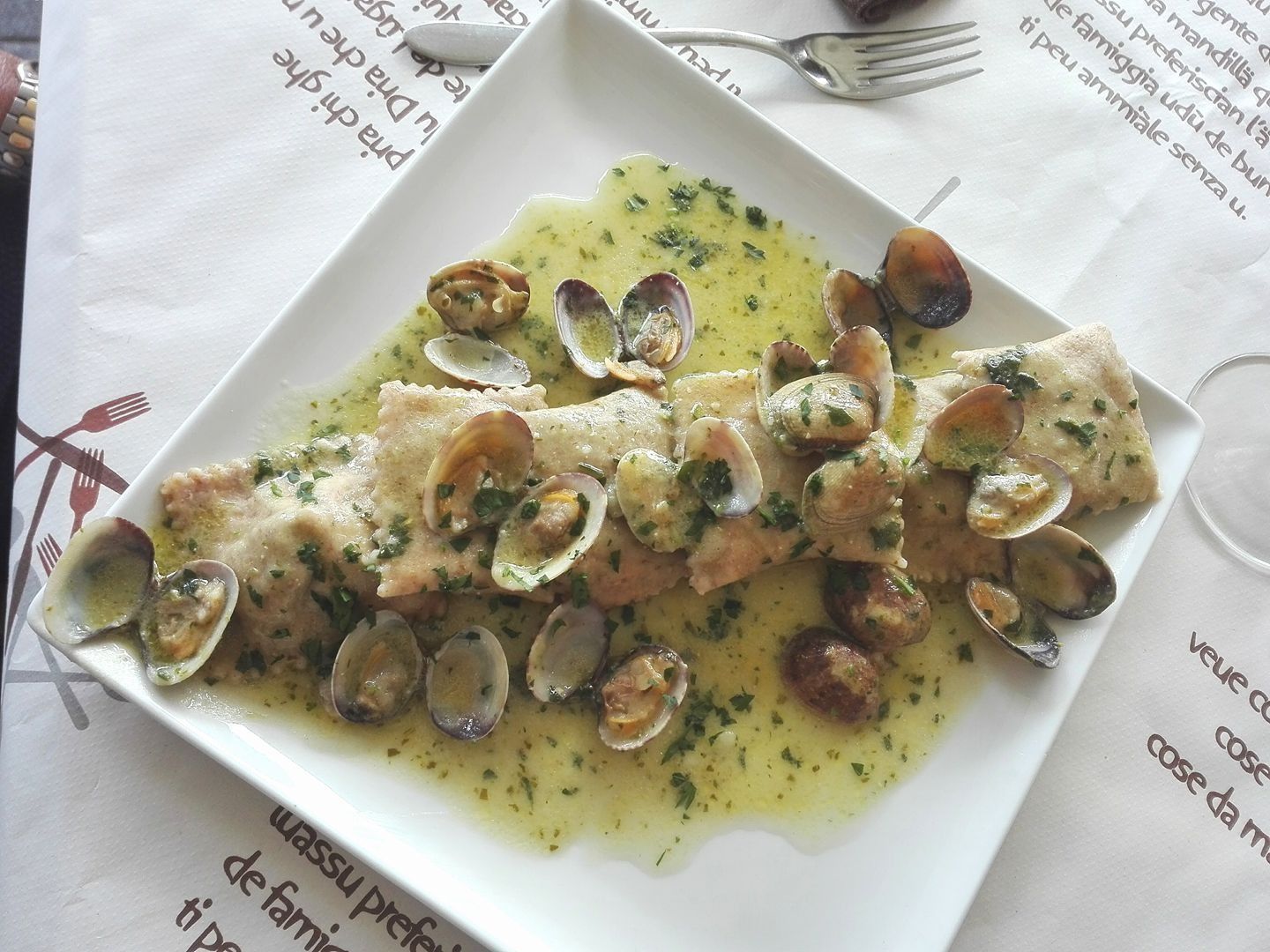 Piatto di pasta con vongole in salsa leggera, servito su un piatto quadrato bianco.