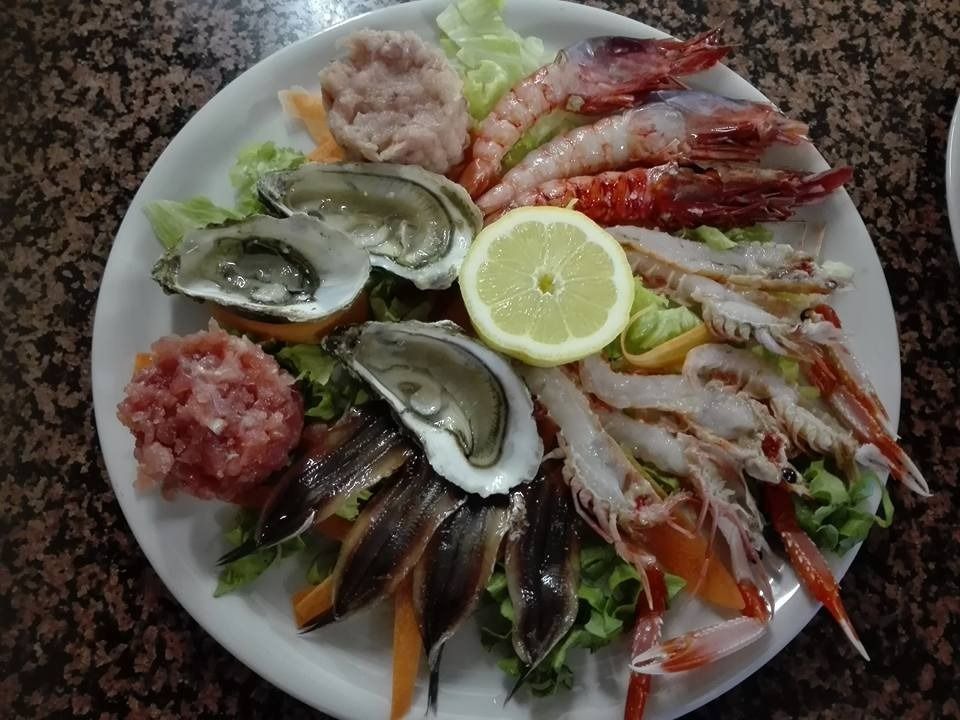 Piatto di frutti di mare con ostriche, gamberi e limone su un piatto bianco.