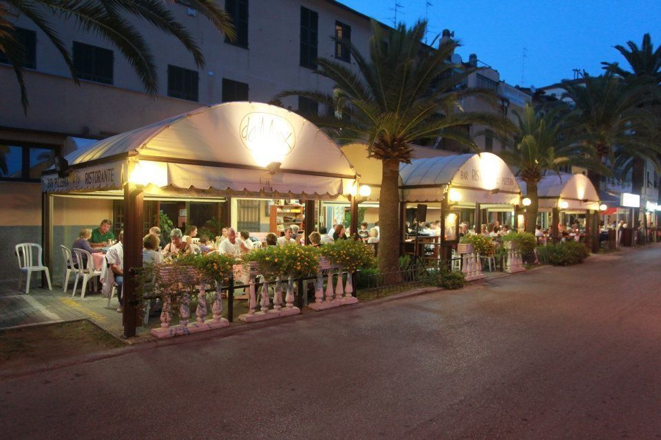 Ristorante all'aperto con tende illuminate e commensali seduti ai tavoli sotto le palme.