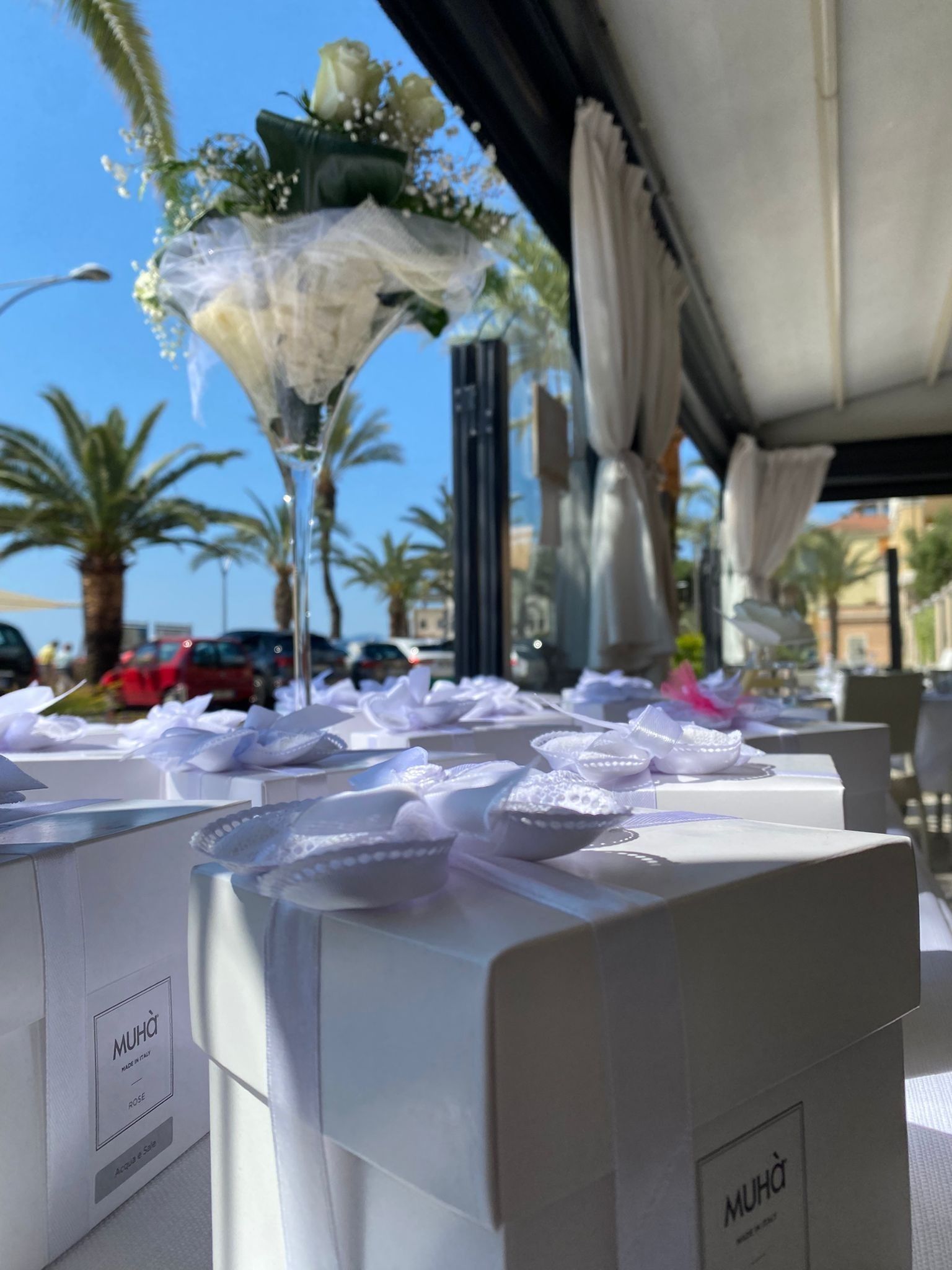 Composizione floreale bianca su un tavolo con scatole bianche, vista sull'oceano, giornata di sole.