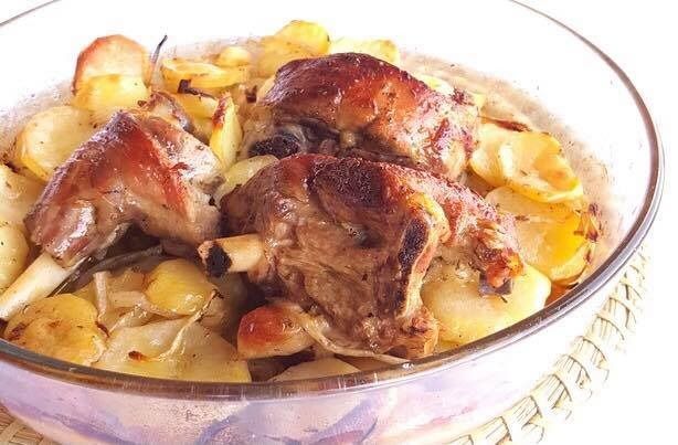 Stinco di agnello arrosto e patate in una teglia di vetro.