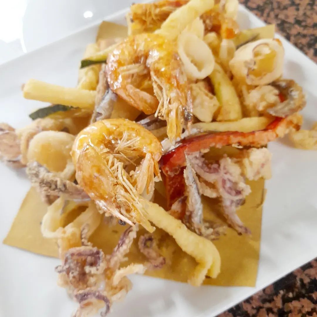 Piatto di pesce fritto su un piatto bianco: gamberi, calamari e verdure.