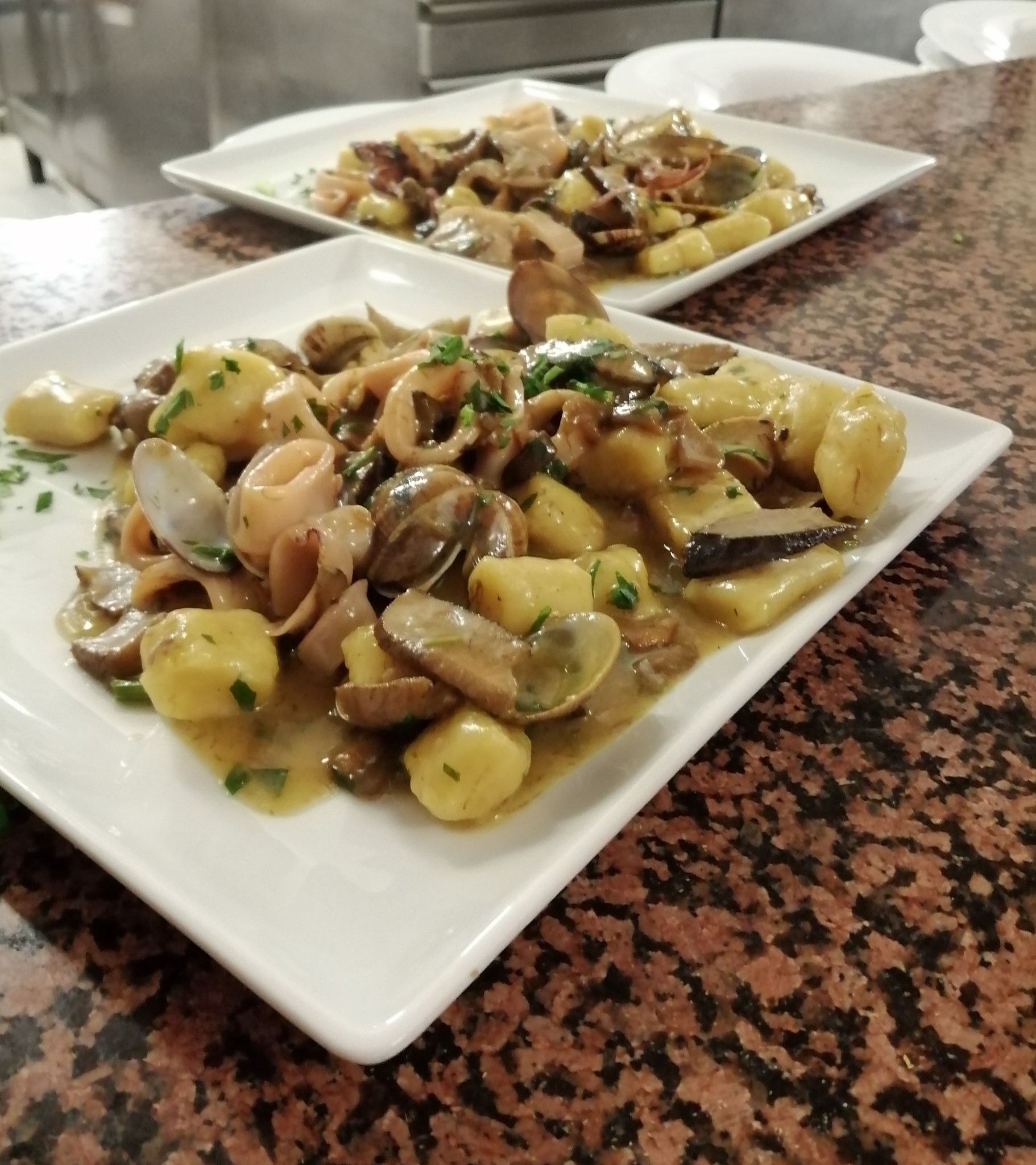 Persona che taglia i pomodori su un tagliere; in primo piano una padella con il cibo.