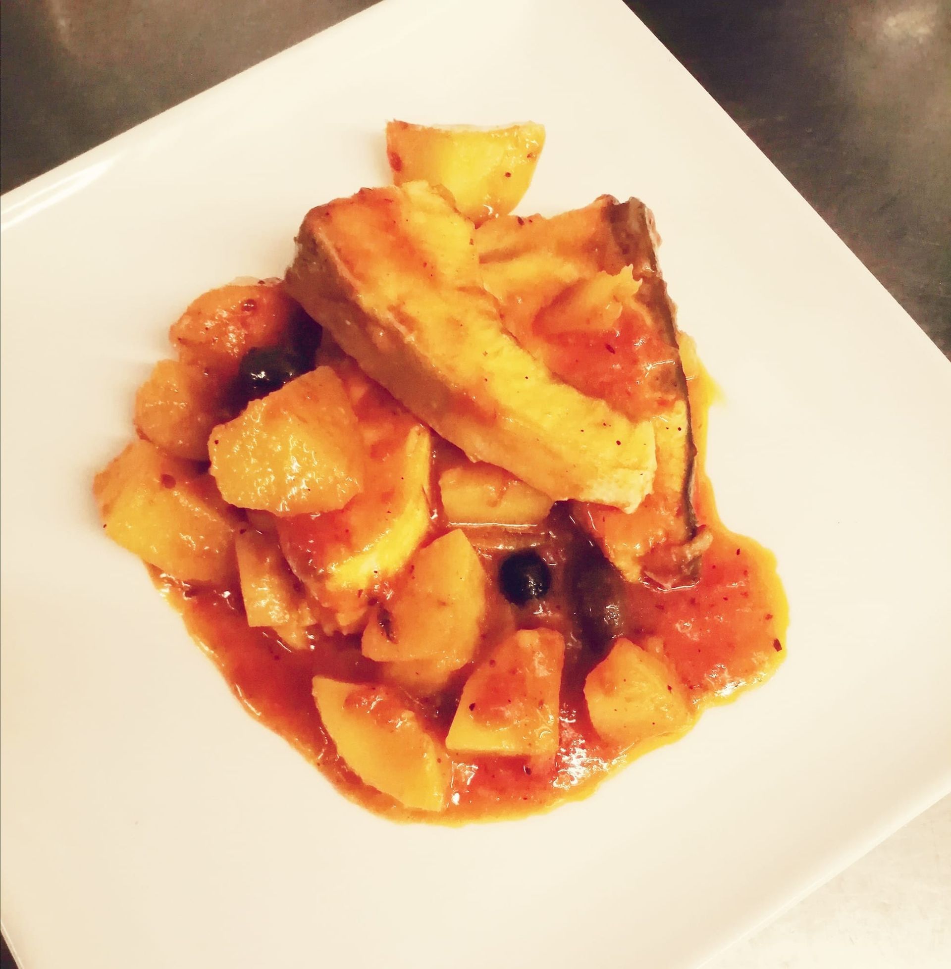 Pesce e patate in salsa di pomodoro, serviti su un piatto bianco.