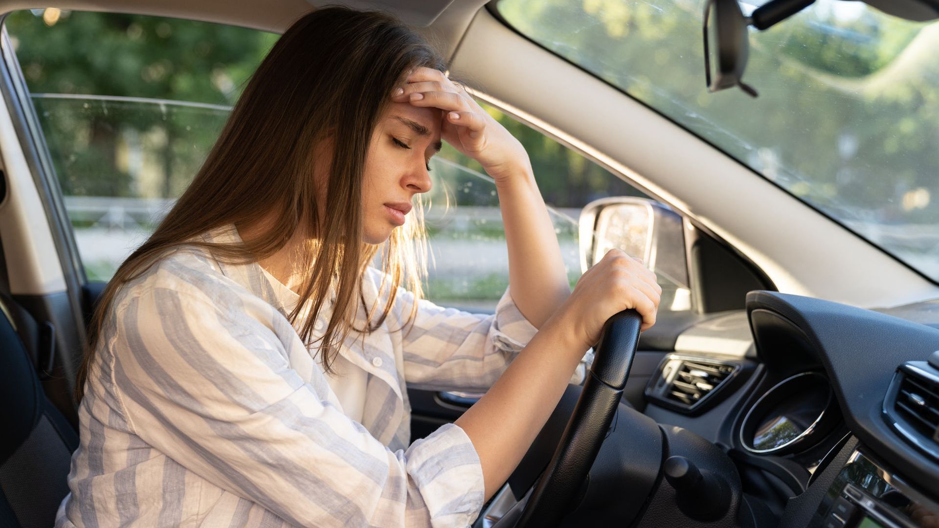 A woman is sitting in a car with her head in her hands.