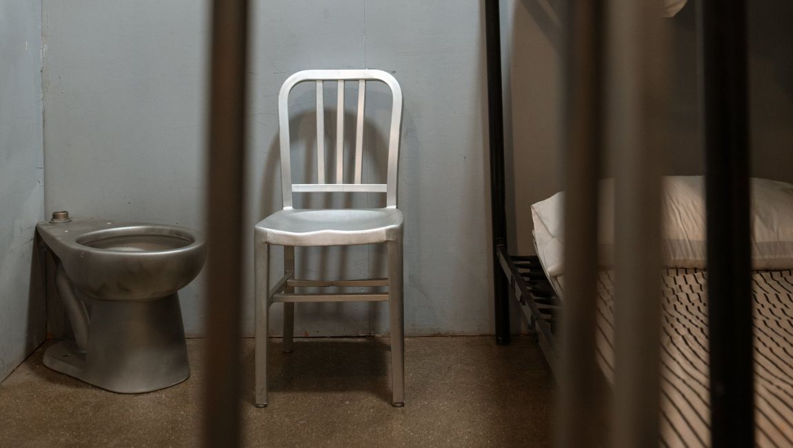 a white chair is sitting in a prison cell next to a toilet .