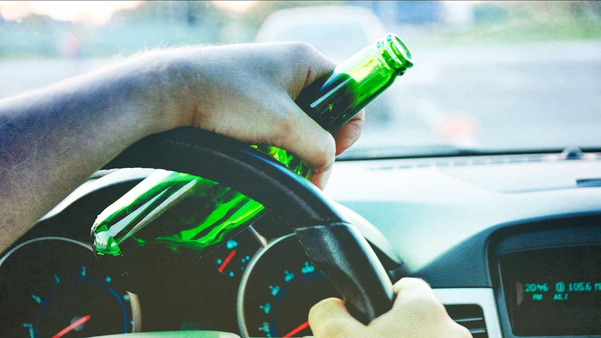 a person is holding a bottle of beer while driving a car .