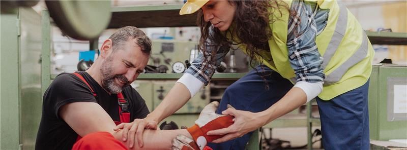 “Construction worker receiving first aid for an injured arm from a safety officer inside an industry