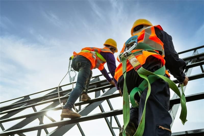 “Construction workers wearing safety harnesses and helmets climbing a steel framework at a job site.