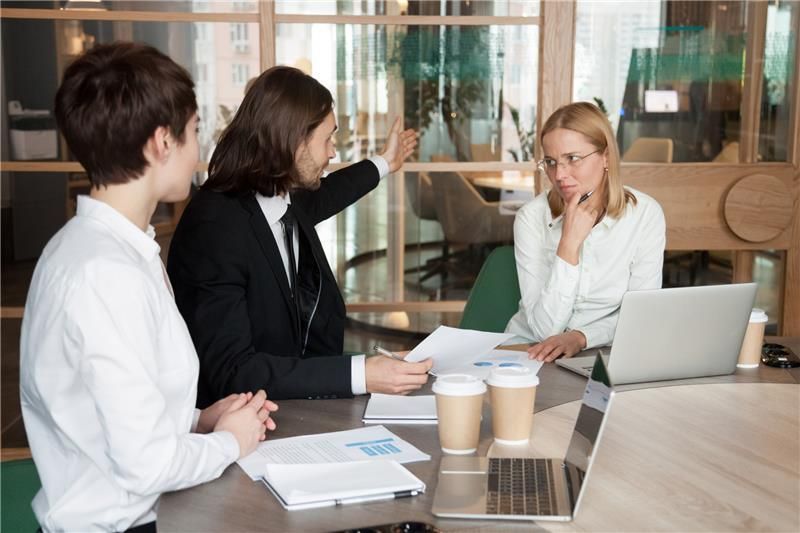 Business professionals in a meeting discussing documents at a conference table with laptops and coff