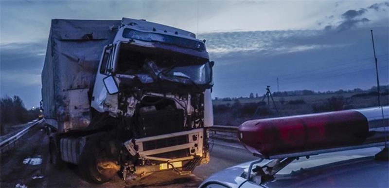 “Damaged semi-truck after a highway accident with a police vehicle and emergency lights in the foreg