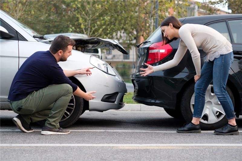 A man and a woman inspecting the damage to the front of a silver car and the rear of a black car