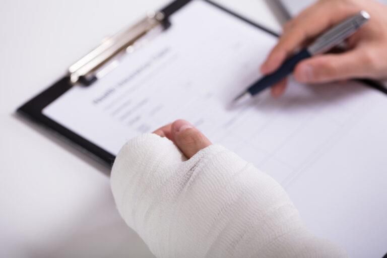 Close-up of a person with a bandaged or casted hand signing a document on a clipboard with their