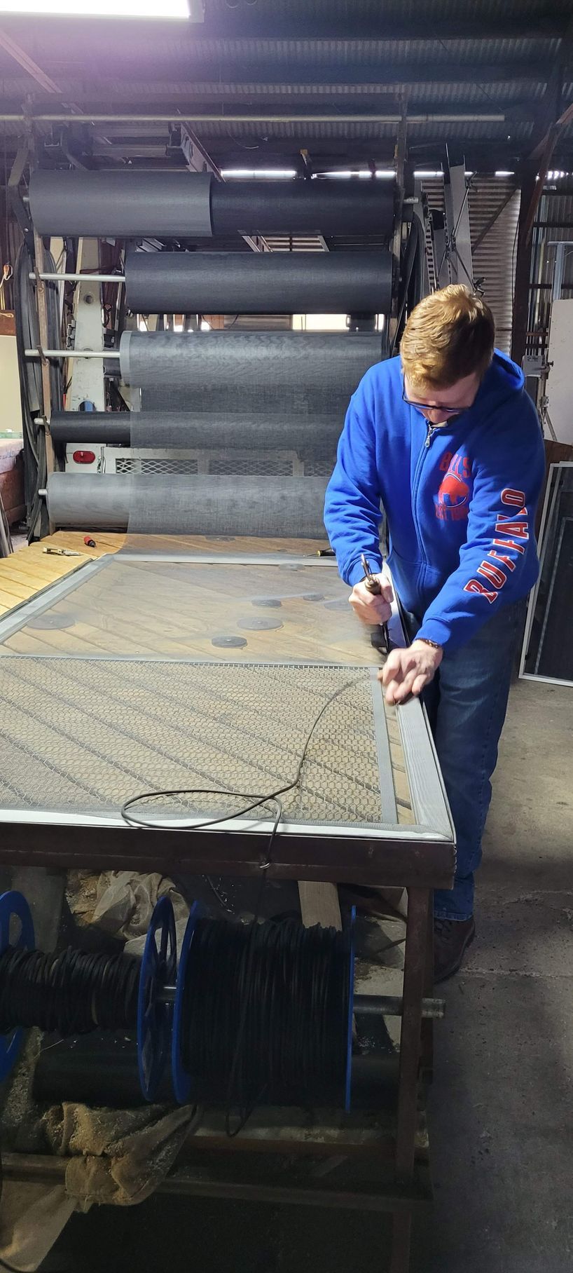 A man in a blue jacket is working on a table in a factory.