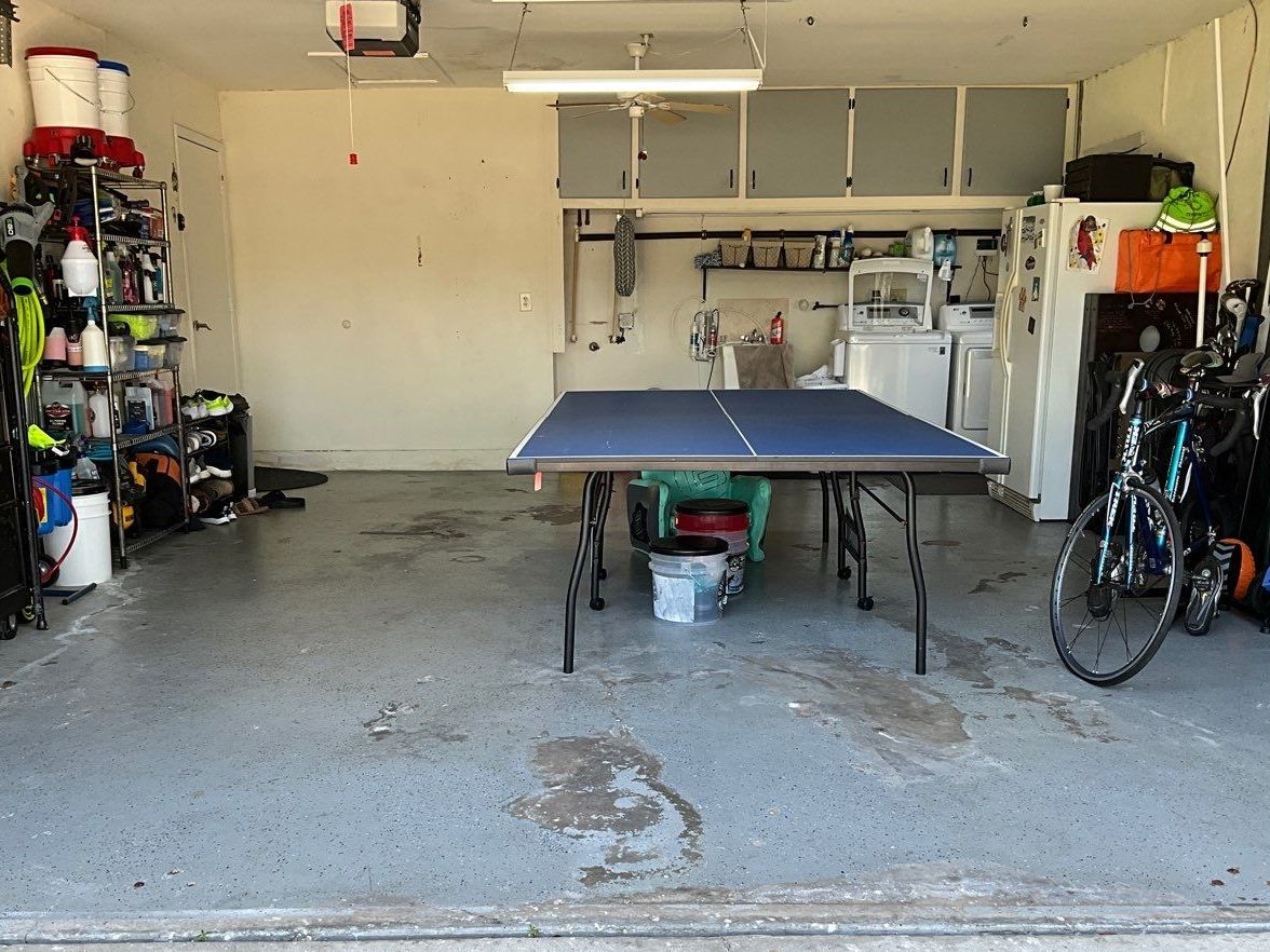 Garage storing ping pong table, biked and other supplies on chipped, stained and dirty concrete floor 