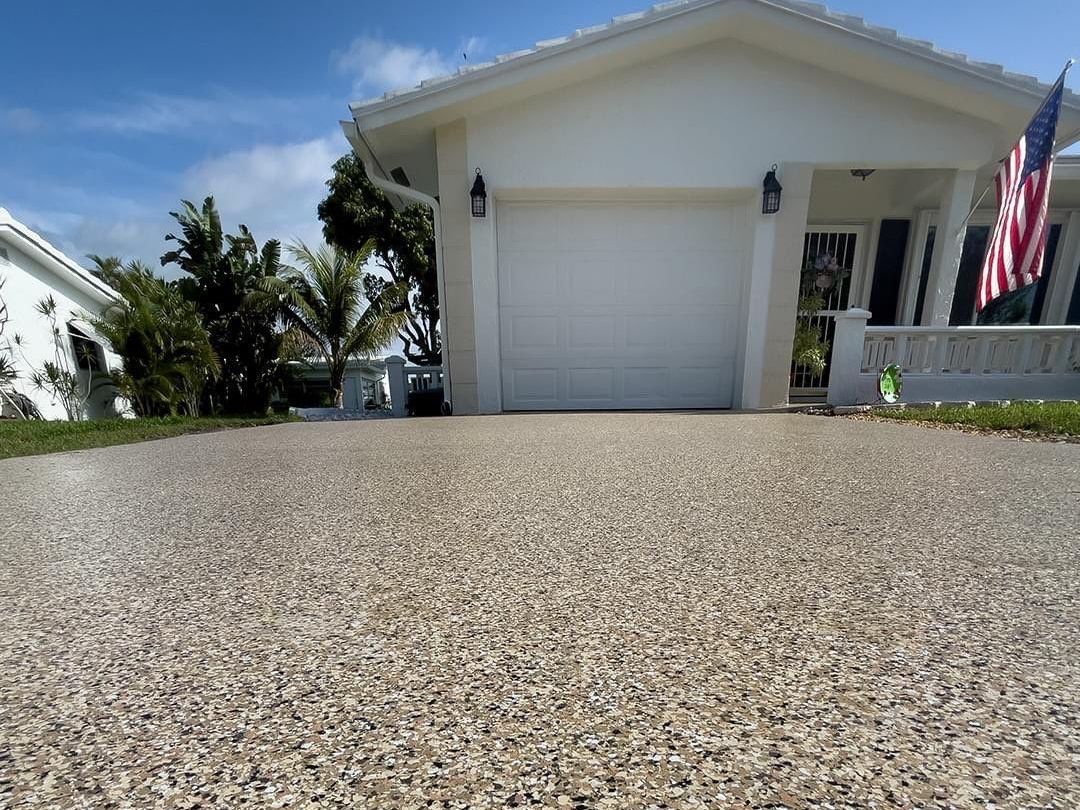 Neutral toned concrete coating on driveway leading up to beige and white house with garage