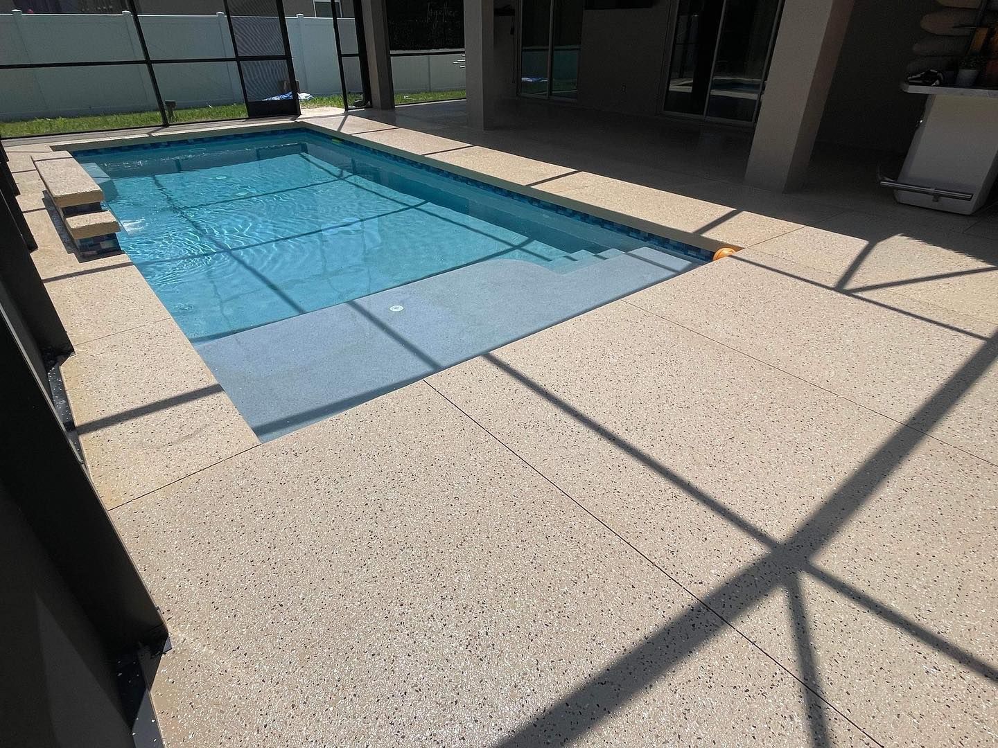 Concrete pool deck coating with warm brown, tan and black flake colors next to a sparkling blue pool