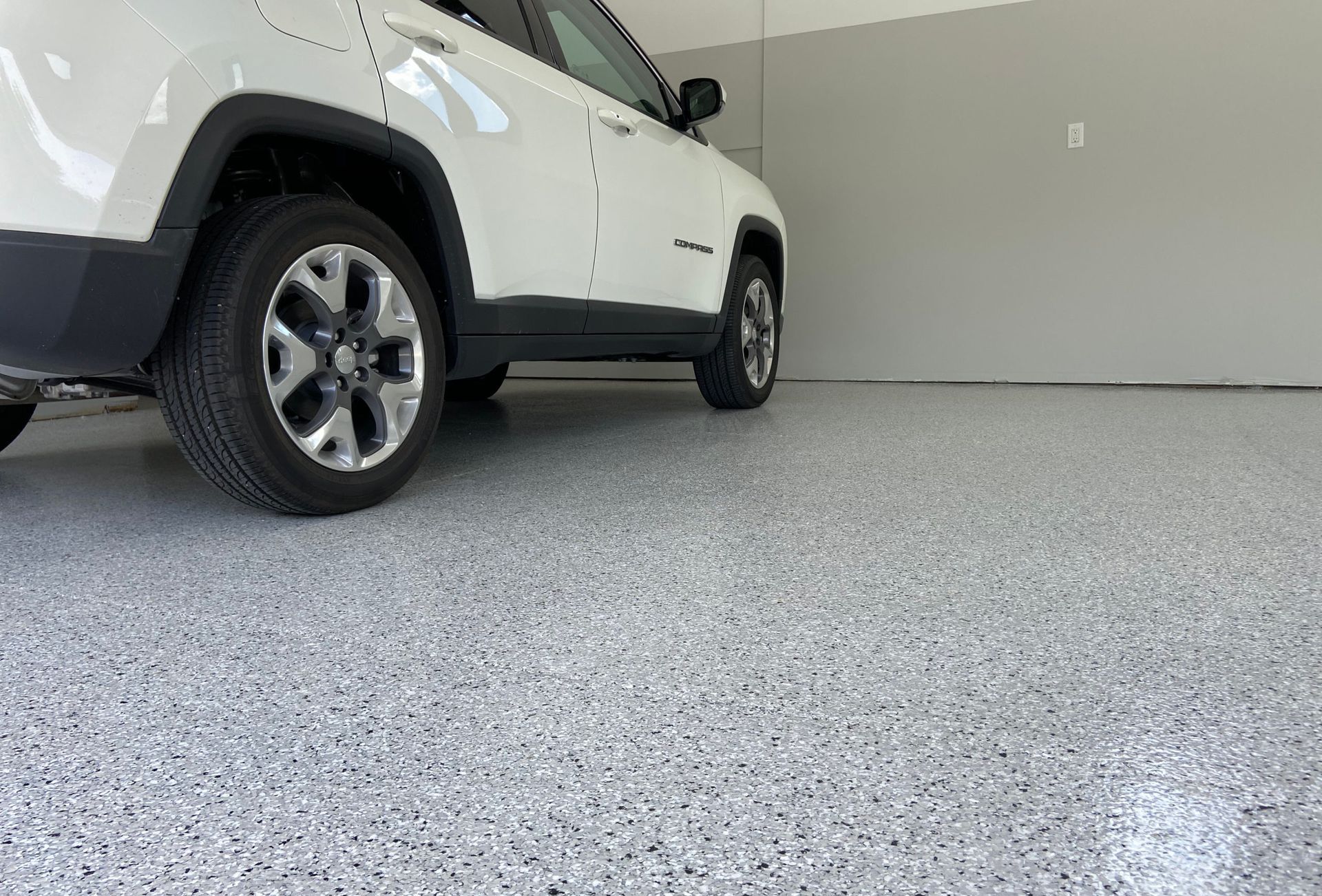 Gleaming blue and grey concrete coating on garage floor beneath the wheel of a parked car.