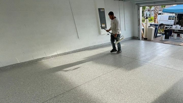 Altantis concrete coating installer using long handled roller and squeegee to apply polyaspartic top coat to garage floor