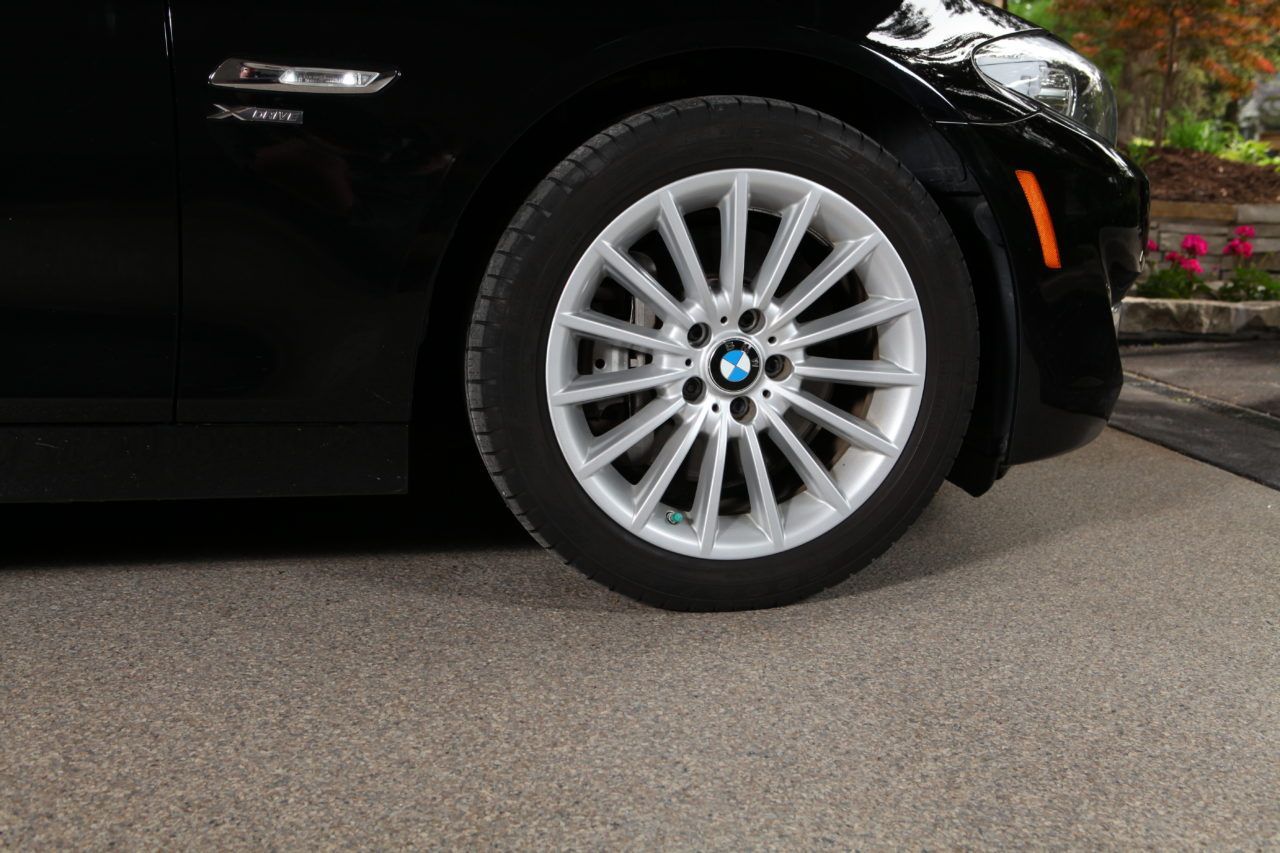 Car wheel with BMW logo parked over concrete driveway with neutral-toned coating