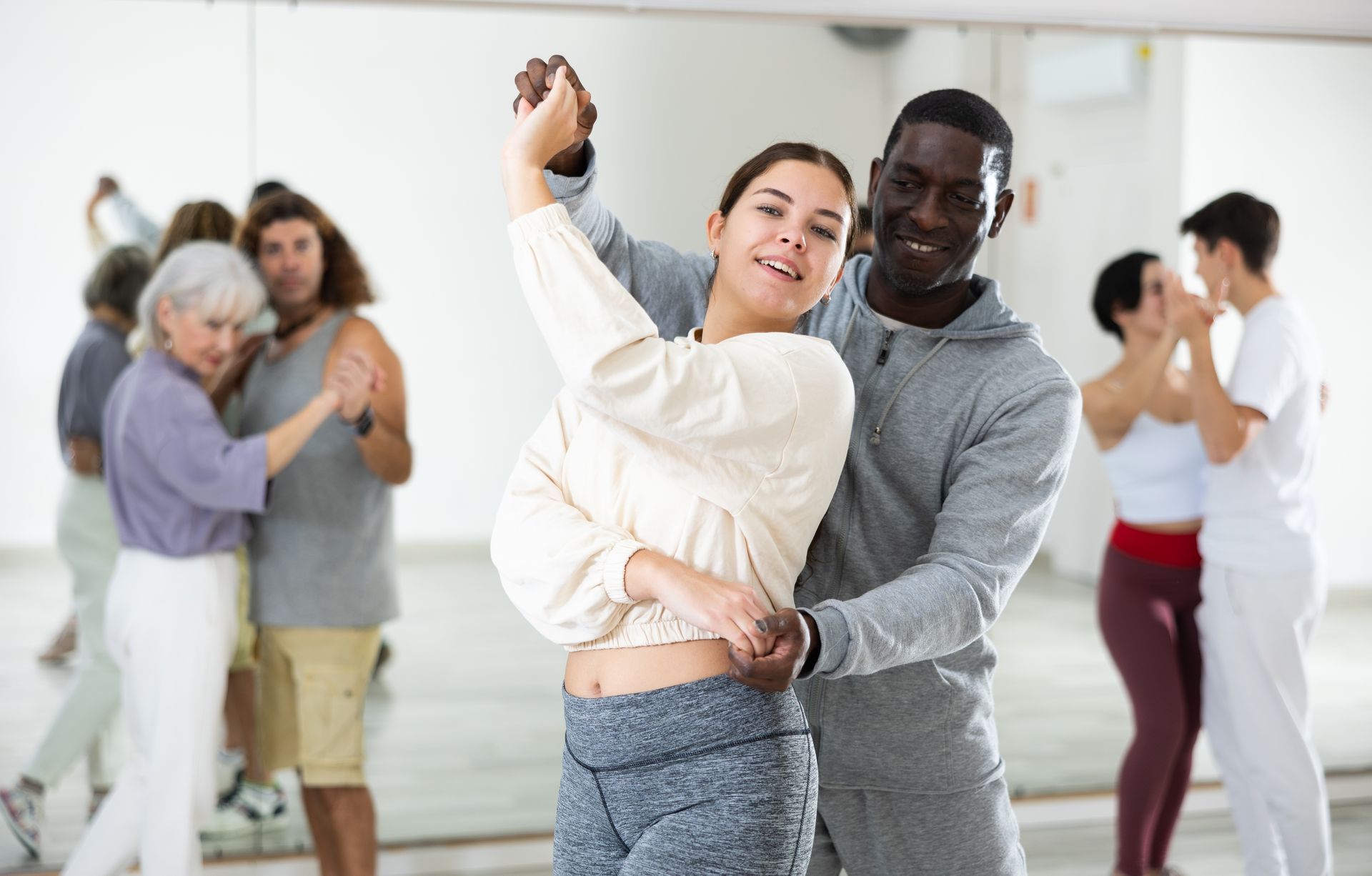 A man and a woman are dancing in front of a mirror in a dance studio.