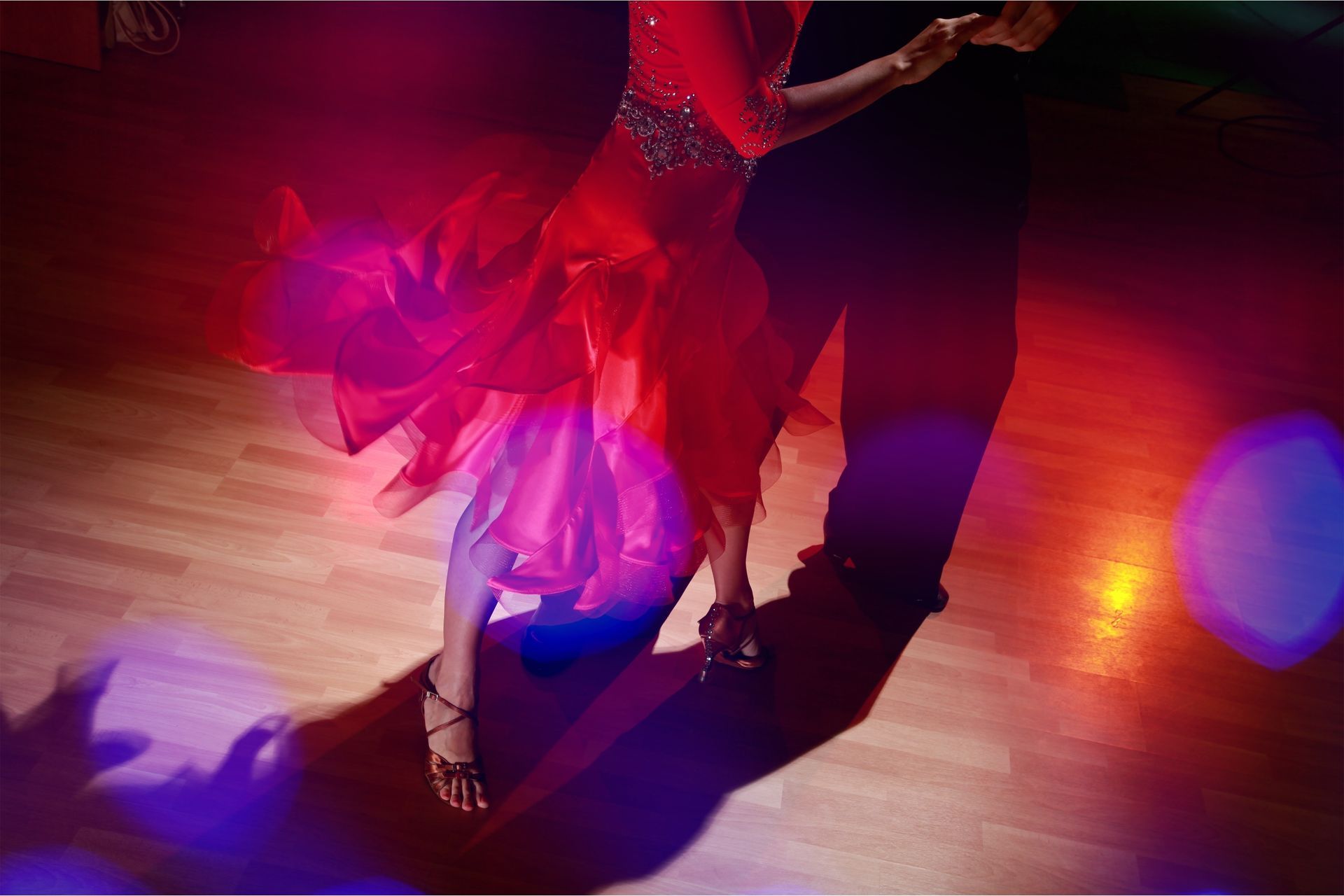 A woman in a red dress is dancing with a man in a black suit on a dance floor.
