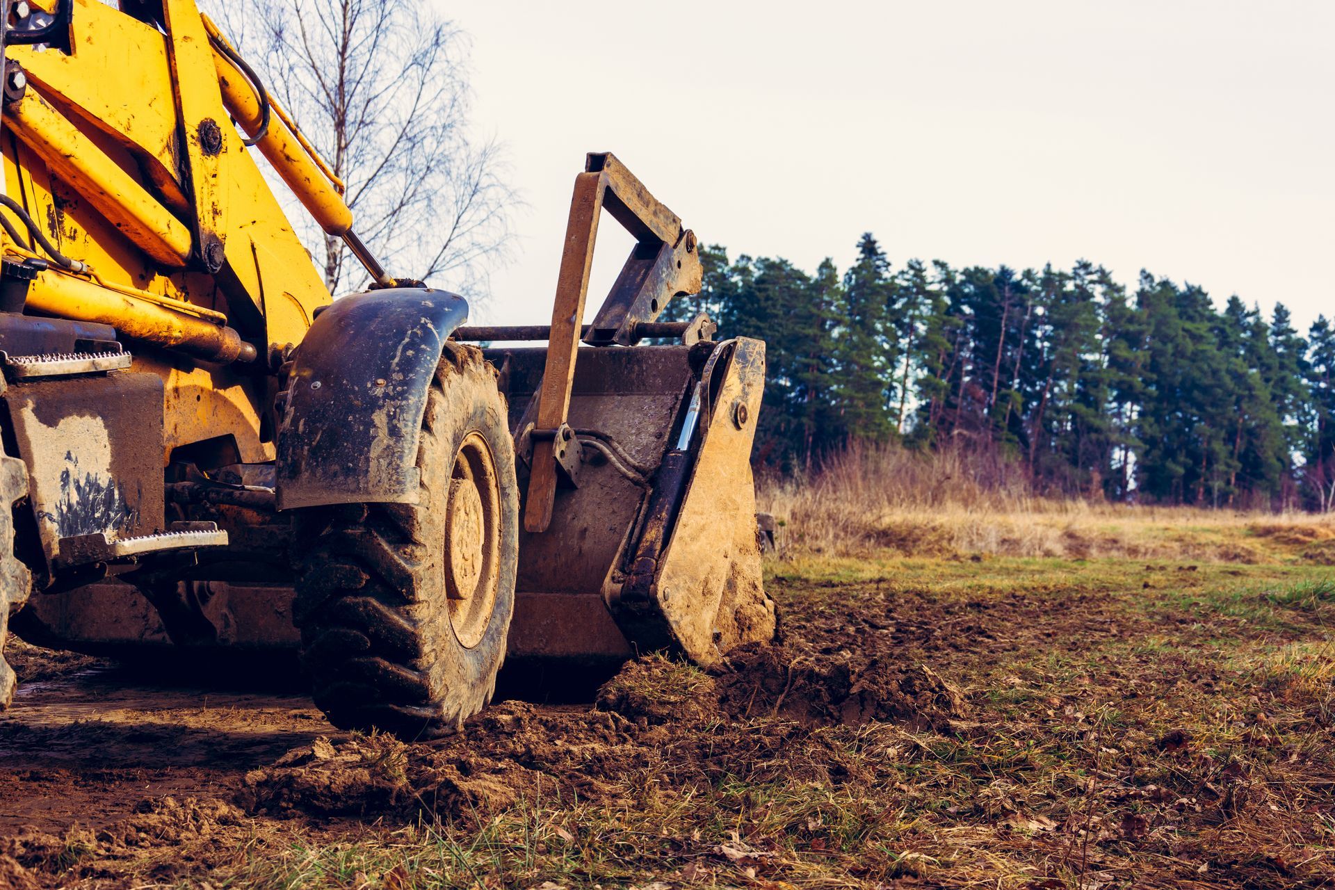 Worker using a grader machine to smooth and level the soil in preparation for the installation of concrete slabs.