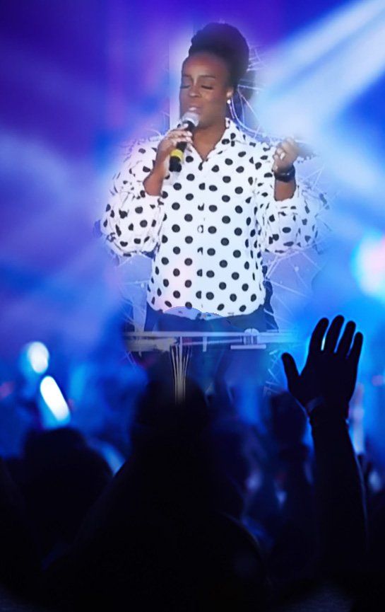 Music minster at Praise fellowship church singing into a microphone on a stage.