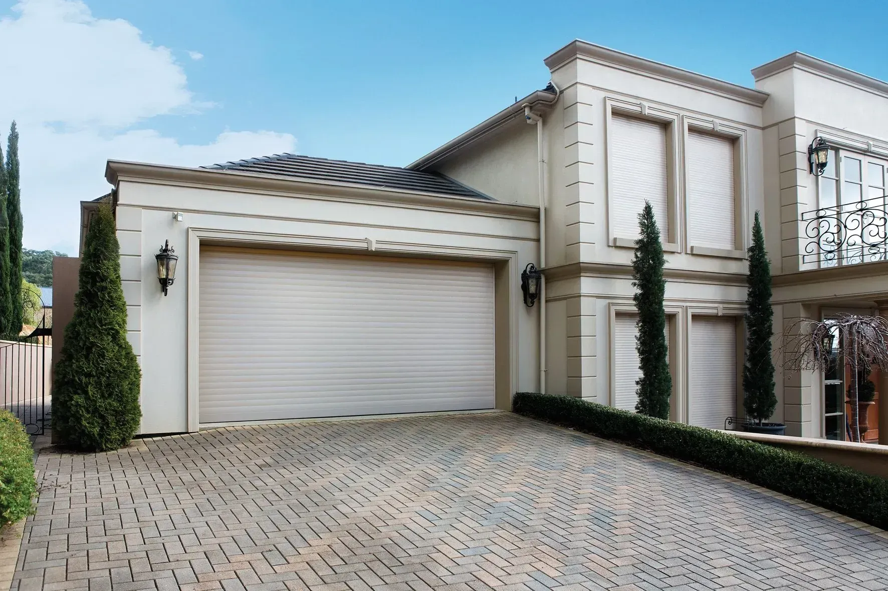 Two windows with closed white roller shutters on a brick building exterior.