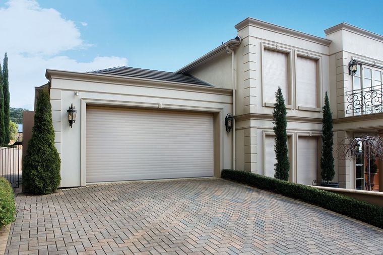 Luxurious beige house with a brick driveway and closed garage door.