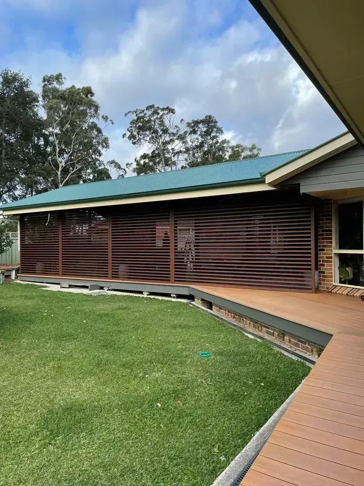 Brown slatted patio with green roof, deck, and grass lawn. Blue sky.