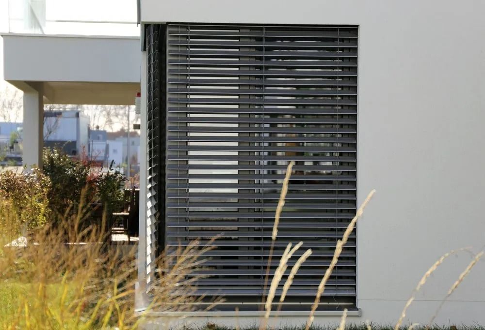 Modern building with closed gray horizontal blinds. Tall grass in the foreground.