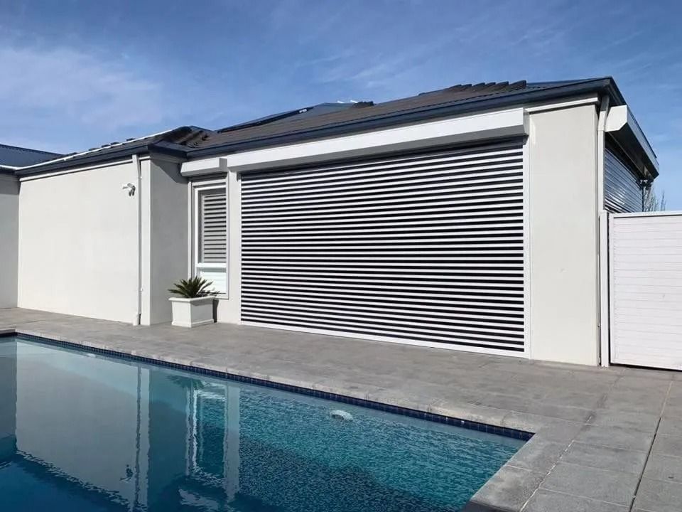 A modern white house with a closed, striped roll-up garage door beside a swimming pool.
