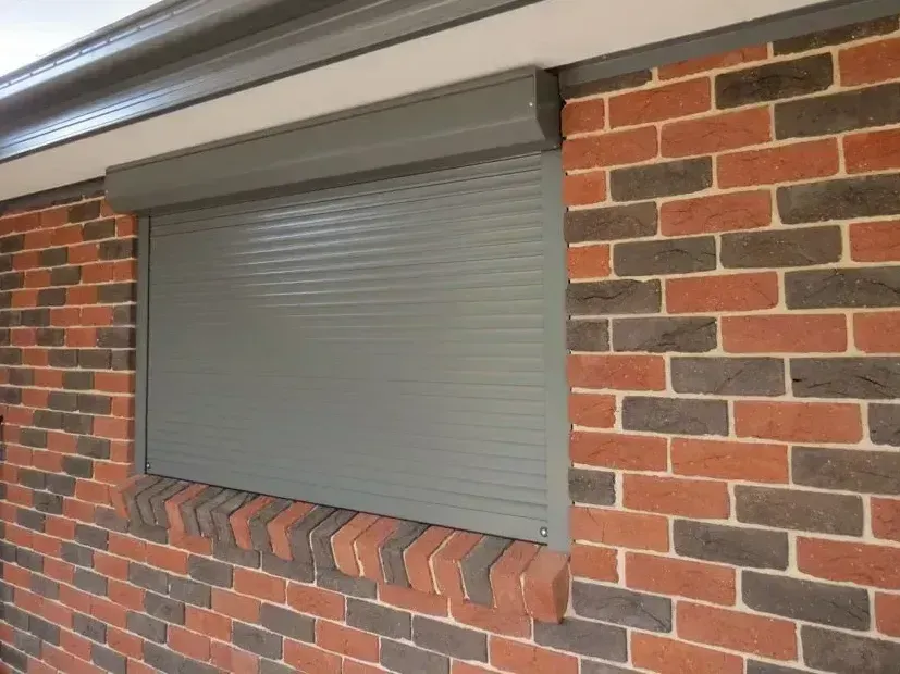 Gray rolling shutter installed on a brick wall over a window.